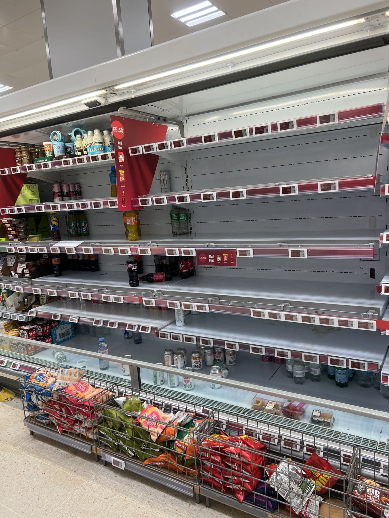 Supermarket fridge shelves with multiple rows almost empty of stock